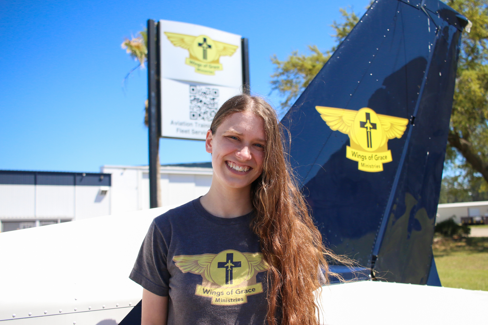 A Wings of Grace student standing beside the tail of a ministry aircraft