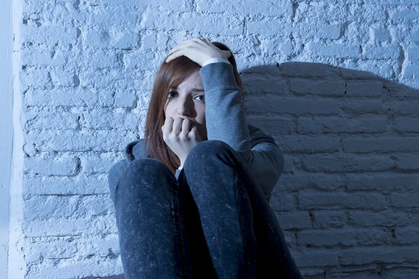 A young woman sitting alone against a brick wall